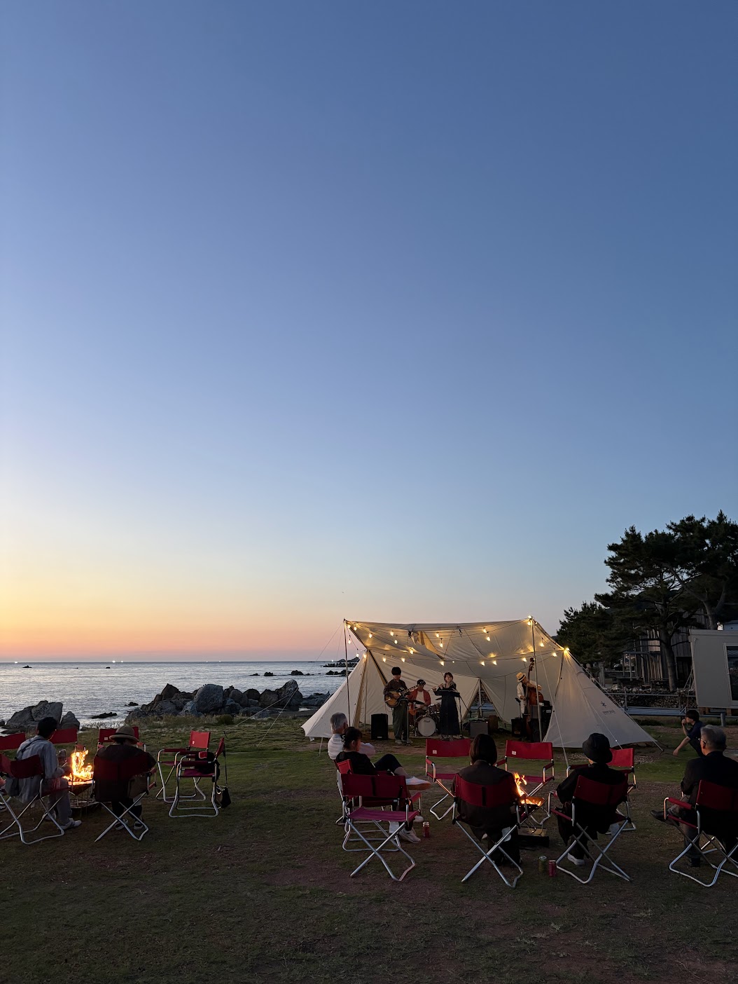 夕暮れの海辺で焚火を囲みながら音楽を楽しむアウトドアイベント