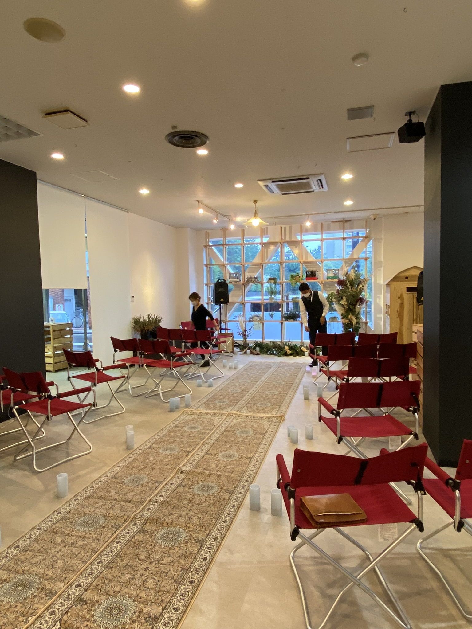 公共の屋内空間に赤いFDチェアと絨毯、装花を配置したウェディング会場